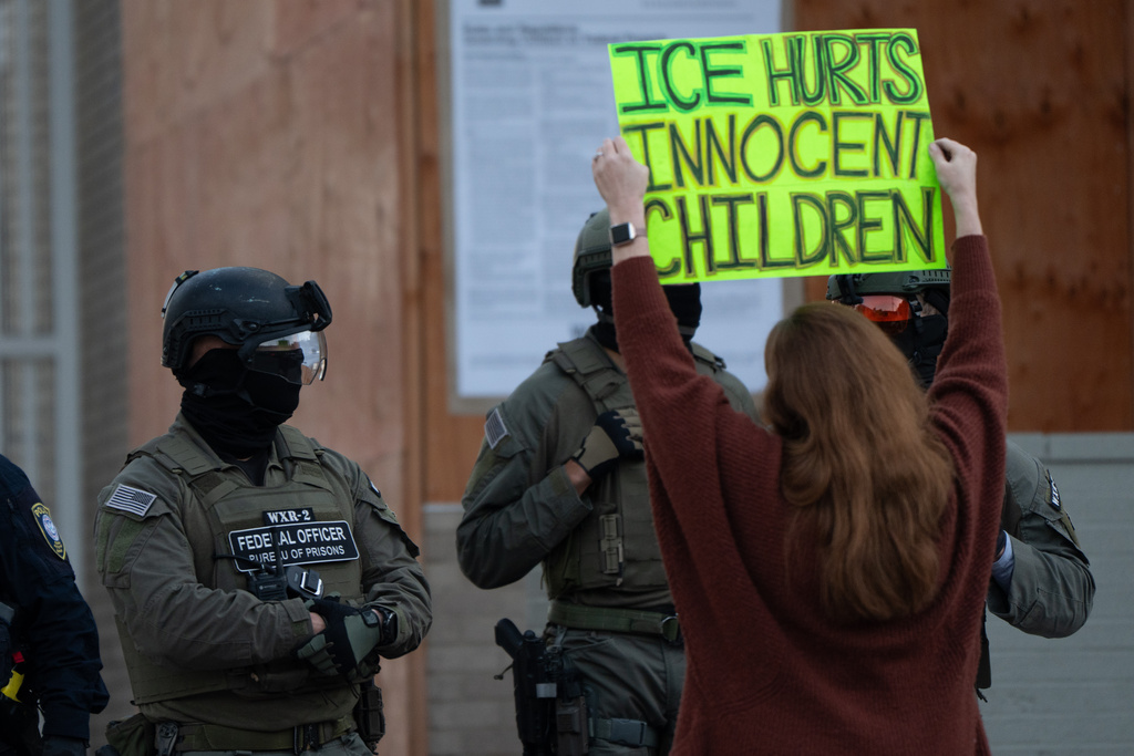 FILE - A protester holds a sign as law enforcement officers stand outside a United States Immigration and Customs Enforcement (ICE) facility in Portland, Ore., on Tuesday, Oct. 21, 2025. (AP Photo/Jenny Kane, File)