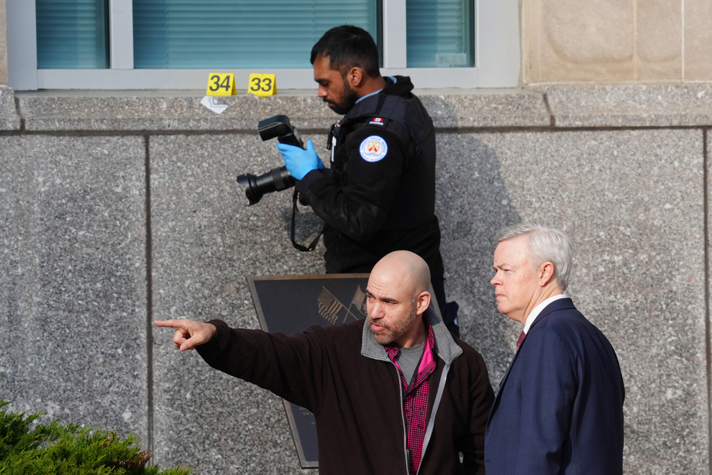 Consulate officials speak together as a Toronto forensic officer photographs bullet impact marks at the front U.S. consulate in Toronto on Tuesday March 10, 2026. (Frank Gunn/The Canadian Press via AP)