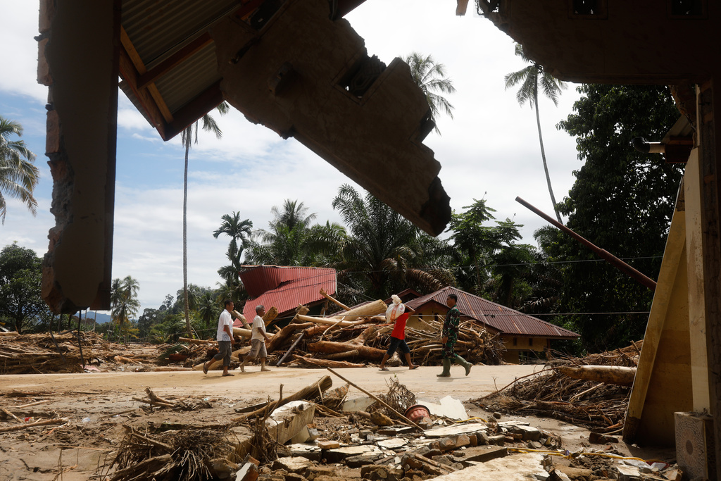 People walk past the ruins of houses at a village affected by flood in Batang Toru, North Sumatra, Indonesia, Wednesday, Dec. 3, 2025. (AP Photo/Binsar Bakkara)