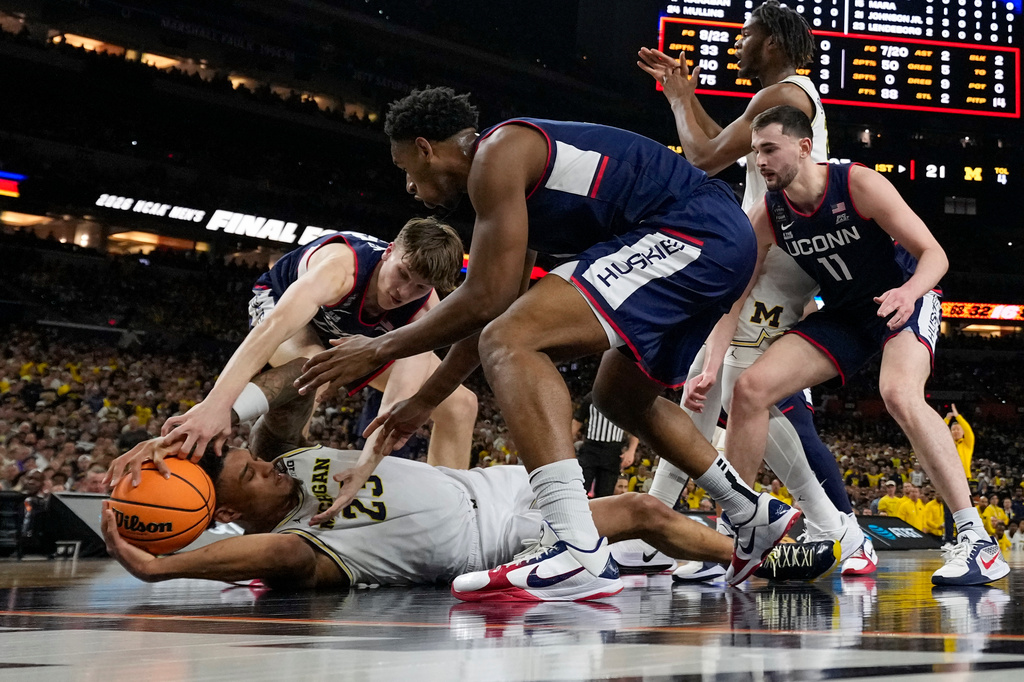 Michigan forward Yaxel Lendeborg is pressured by UConn guard Braylon Mullins, rear, and forward Tarris Reed Jr., right, during the first half of the NCAA college basketball tournament national championship game at the Final Four, Monday, April 6, 2026, in Indianapolis. (AP Photo/Abbie Parr)