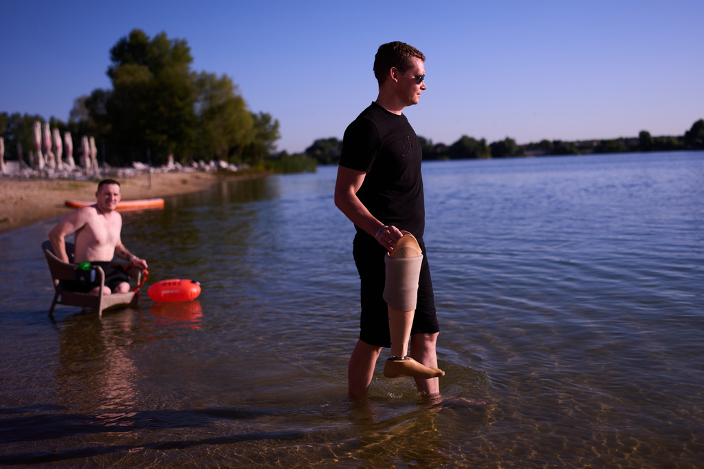 A man holds the prosthetic leg of a Ukrainian war veteran as Maksym Yuzviak, left, also a veteran, sits on a chair during a sporting event to encourage people and injured soldiers to take part in sports at a lake on the outskirts of Kyiv, Monday, Aug. 24, 2026, during the 35th anniversary of Ukraine's Independence Day. (AP Photo/Francisco Seco) Corrects spelling of Maksym Yuzviak, not Maxim Yuzvyak