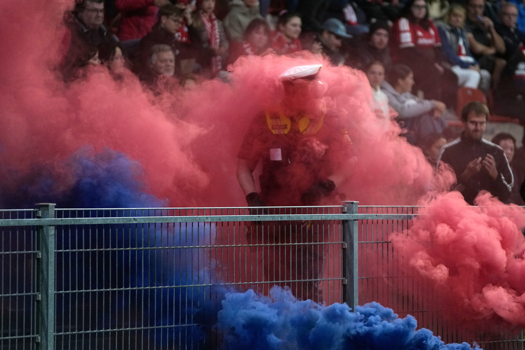 A policeman is engulfed in colored smoke from smoke bombs thrown onto the pitch during the women's Champions League opening phase soccer match between FC Bayern Munich and Manchester City in Munich, Germany, Tuesday, Sept. 22, 2026. (AP Photo/Matthias Schrader)