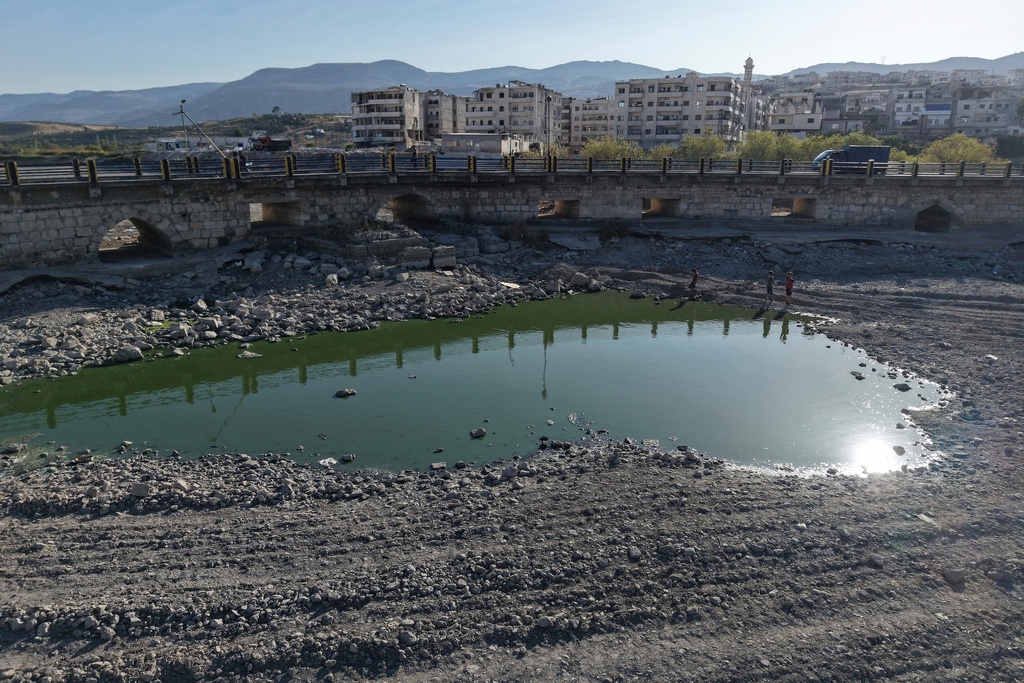 FILE - Boys stand next to the dried up Orontes River, the result of a drought following heat waves and a winter with very little precipitation, in Jisr al-Shughur, west of Idlib, Syria, Aug. 14, 2025. (AP Photo/Omar Albam, File)