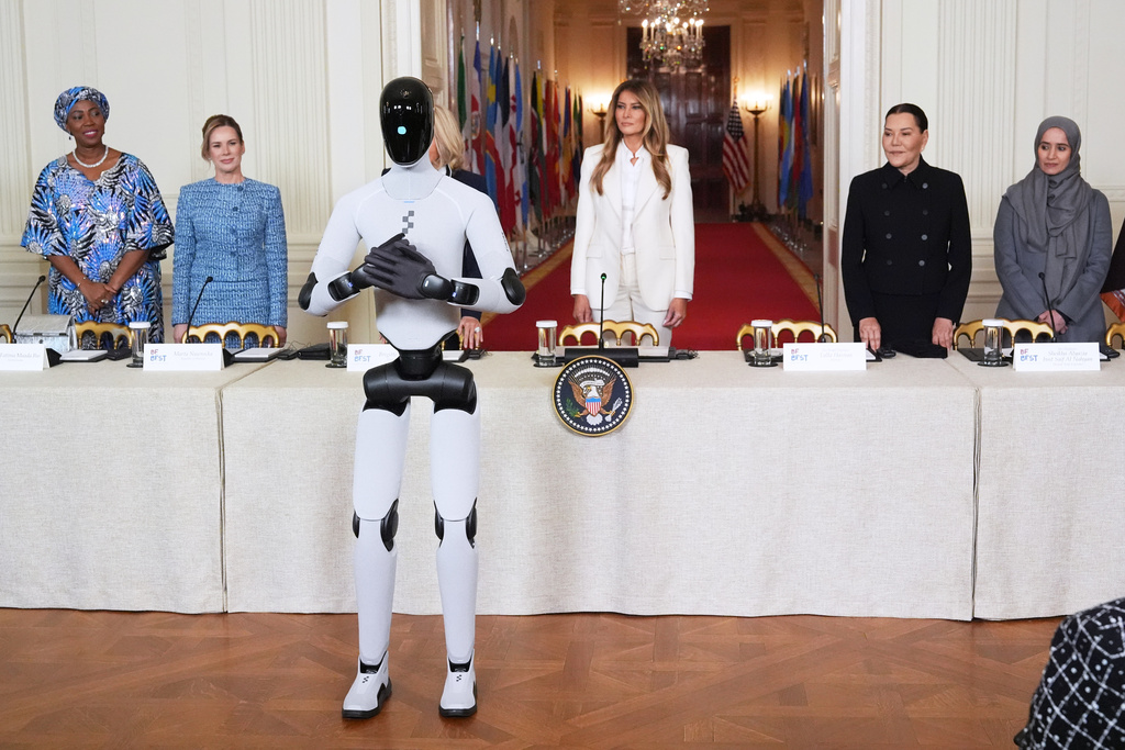 First lady Melania Trump arrives, accompanied by a robot, to attend the "Fostering the Future Together Global Coalition Summit," with other first spouses, at the White House, Wednesday, March 25, 2026, in Washington. From left are Dr. Fatima Maada Bio, of Sierra Leone, Martha Nawrocka of Poland, Brigitte Macron of France, Melania Trump, Her Royal Highness Lalla Hasnaa of Morocco and Her Highness Sheikha Alyazia bint Saif Al Nahyan of the UAE. (AP Photo/Jacquelyn Martin)