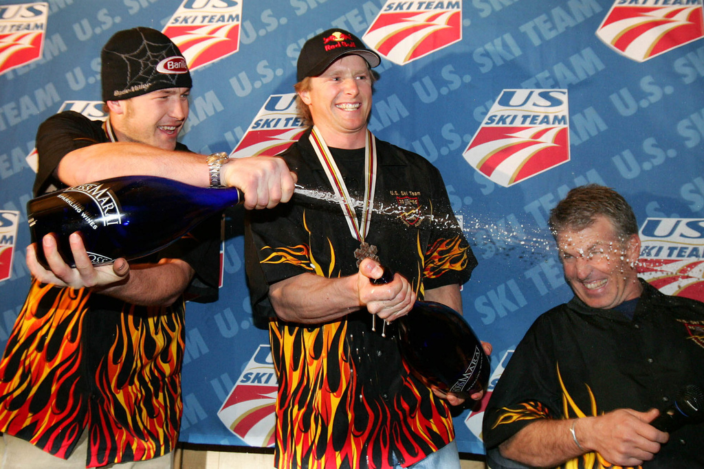 FILE - U.S. skier Bode Miller, left, sprays sparkling wine on Phil McNichol, head coach of the U.S. men's alpine ski team, as Daron Rahlves, center, smiles during a victory party in the American House in Bormio, Italy, Feb. 5, 2005. (AP Photo/Thomas Kienzle, File)