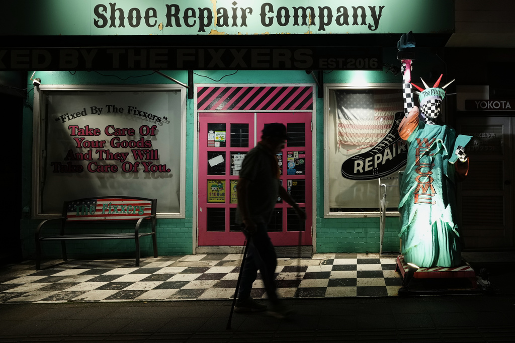 A man walks past The Fixxers shoe repair shop, decorated with a sculpture with a unique painting imitating the Statue of Liberty, in Fussa, west of Tokyo, Saturday, June 27, 2026. (AP Photo/Hiro Komae)