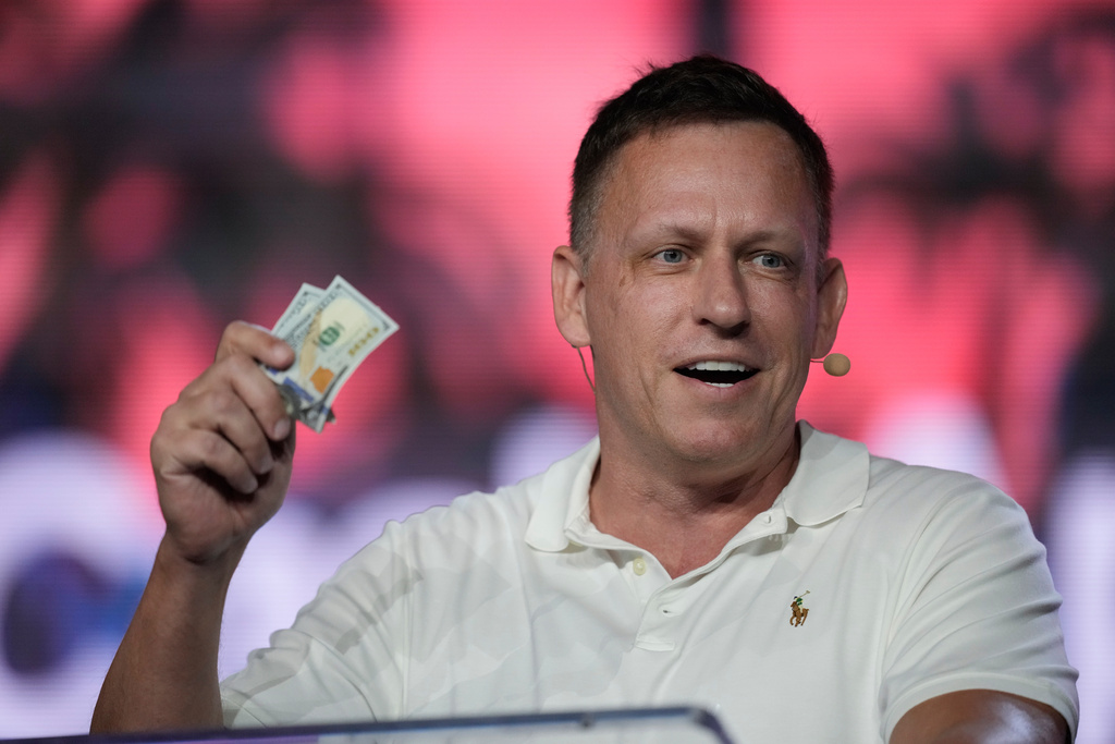 FILE - Peter Thiel, co-founder of PayPal and Palantir, offers a pair of hundred dollar bills to attendees during a keynote address at the Bitcoin Conference, April 7, 2022, in Miami Beach, Fla. (AP Photo/Rebecca Blackwell, File)