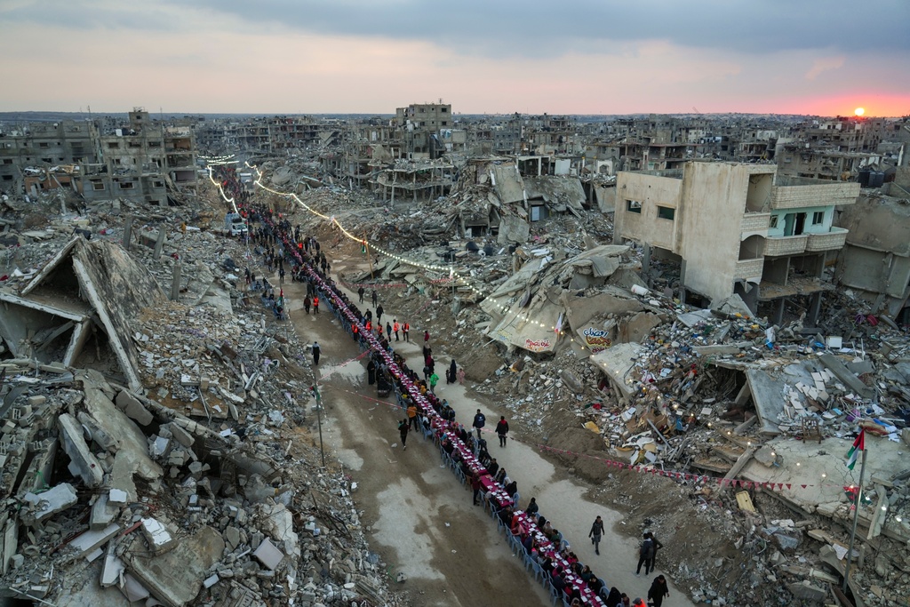 Palestinians sit at a large table surrounded by the rubble of destroyed homes and buildings as they gather for iftar, the fast-breaking meal, as the sun sets, on the first day of Ramadan, in Rafah, southern Gaza Strip, March 1, 2025. (AP Photo/Abdel Kareem Hana, File)