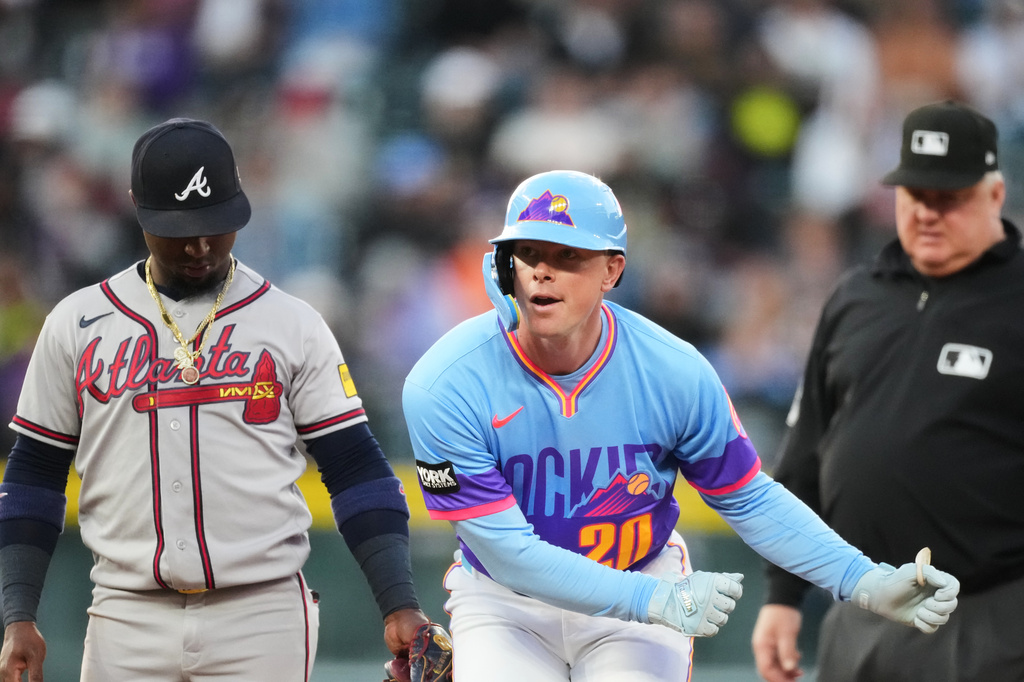 Colorado Rockies'Troy Johnston, center, gestures to the dugout after reaching second base on a double as Atlanta Braves second baseman Ozzie Albies, left, and second base umpire Bill Miller look on in the third inning of a baseball game Friday, May 1, 2026, in Denver. (AP Photo/David Zalubowski)