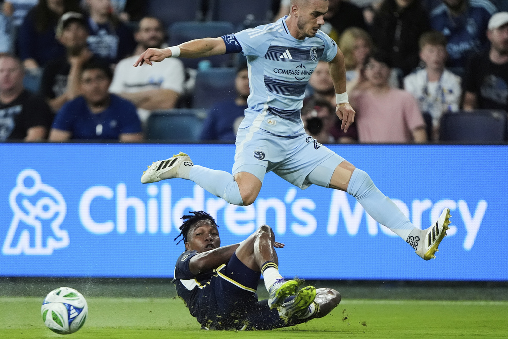 Sporting Kansas City midfielder Erik Thommy, top, leaps over Vancouver Whitecaps defender Edier Ocampo during the first half of an MLS soccer match Saturday, Sept. 20, 2025, in Kansas City, Kan. (AP Photo/Charlie Riedel)