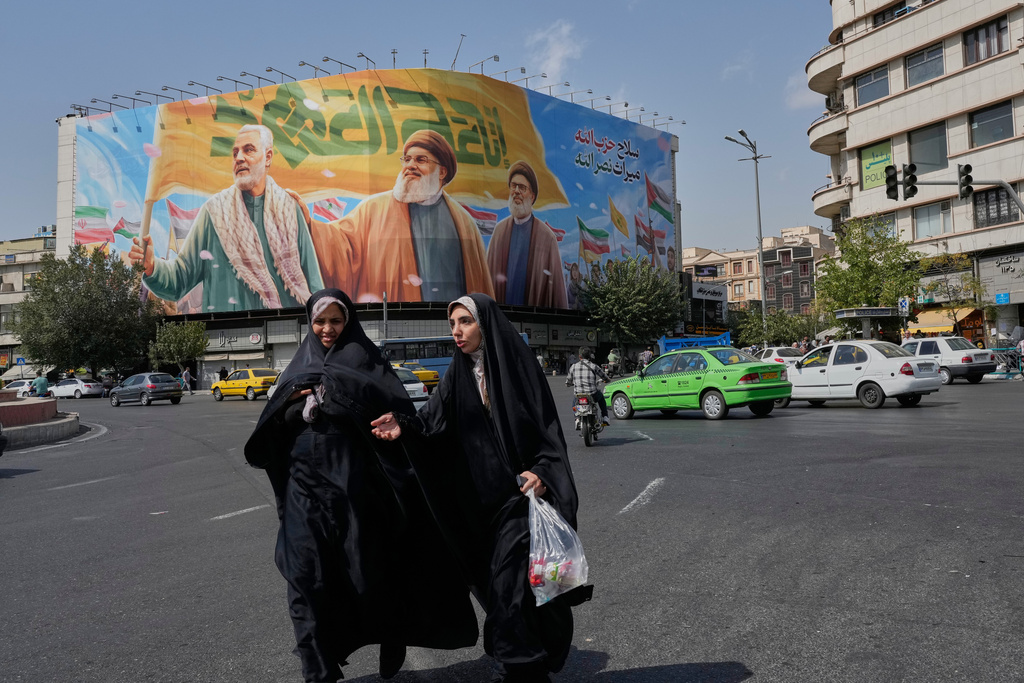 Two women walk past a huge banner showing the late commander of the Iran's Revolutionary Guard expeditionary Quds Force, Gen. Qassem Soleimani, who was killed in a U.S. drone attack in 2020, and two late Hezbollah leaders Hassan Nasrallah, center, and Hashem Safieddine, who were killed in Israeli airstrikes in 2024, at the Enqelab-e-Eslami (Islamic Revolution) square, in Tehran, Iran, Saturday, Sept. 27, 2025. (AP Photo/Vahid Salemi)