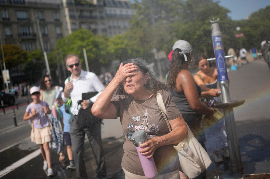FILE - Tourists cool off at a public water fountain in Paris, June 26, 2026. (AP Photo/Christophe Ena, File)