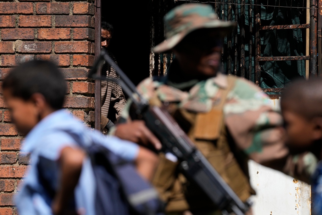 A man watches on South African National Defense Force officers patrolling the street in the Westbury township of Johannesburg, South Africa, Wednesday, March 11, 2026. (AP Photo/Themba Hadebe)
