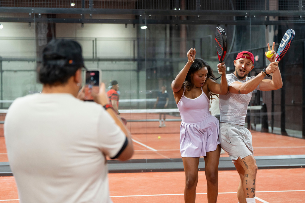 Lehi Castaneda takes a video of Phoenix-based content creator Aiesha Beasley and her boyfriend Jonah Downey during the grand opening of Padeland, a venue for the racket sport padel in Chandler, Ariz., Thursday, Aug. 13, 2026. (AP Photo/Rebecca Noble)