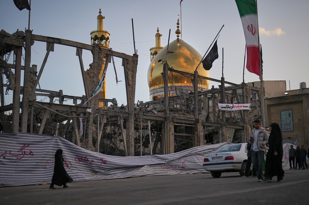 Pedestrians walk by a destroyed building within the Grand Hosseiniyeh, with the mosque visible in the background, which officials at the site say was hit by U.S.-Israeli airstrikes Tuesday, in Zanjan, Iran, Saturday, April 4, 2026. (AP Photo/Francisco Seco)
