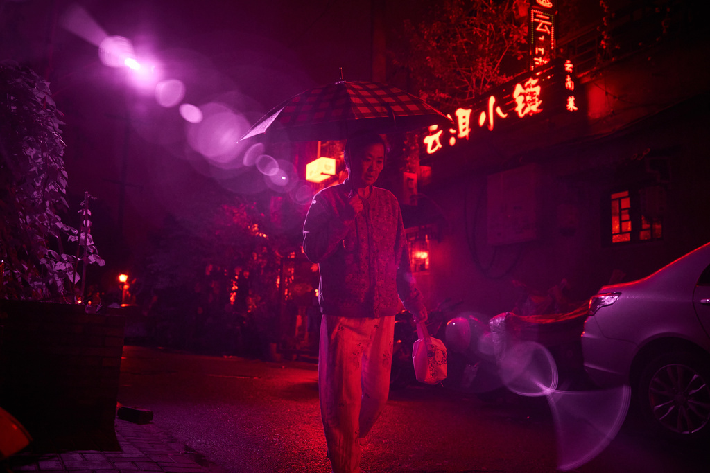 An infrared beam of light shines from a security camera watching over the Beigulou alleyway in Beijing as a pedestrian passes, Oct. 9, 2025. (AP Photo/Ng Han Guan)