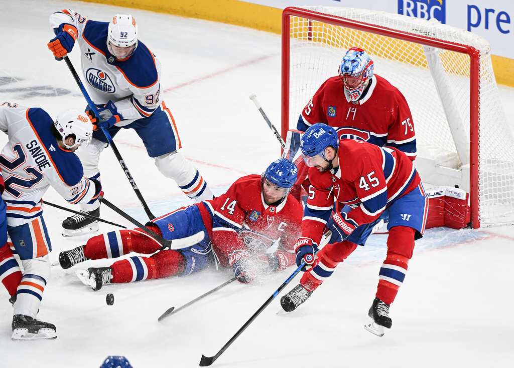Montreal Canadiens goaltender Jakub Dobes (75) looks on as Canadiens' Nick Suzuki (14) blocks a shot by Edmonton Oilers' Matt Savoie (22) as Canadiens' Alexandre Carrier (45) and Oilers' Vasily Podkolzin (92) move in during the first period of an NHL hockey game, in Montreal, Sunday, Dec. 14, 2025. (Graham Hughes/The Canadian Press via AP)