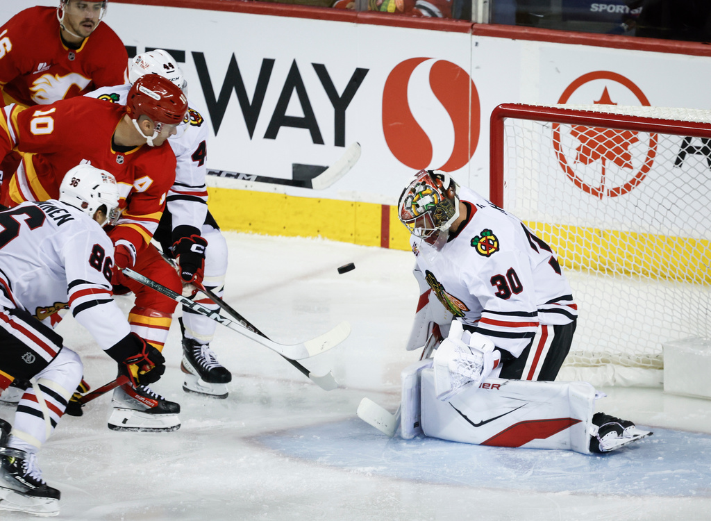 Chicago Blackhawks goalie Spencer Knight, right, stares down the puck as Calgary Flames' Jonathan Huberdeau digs for a rebound during second period NHL hockey action in Calgary, Friday, Nov. 7, 2025. (Jeff McIntosh/The Canadian Press via AP)