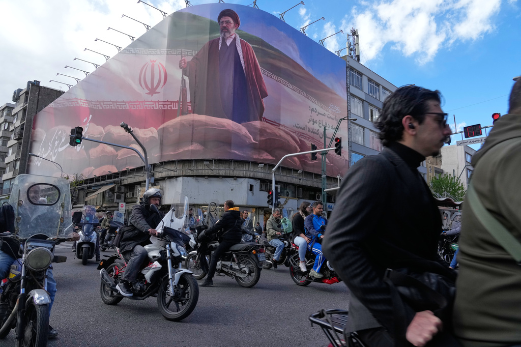 People drive their motorbikes past a billboard that shows a graphic depicting Iran's Supreme Leader Ayatollah Mojtaba Khamenei in downtown Tehran, Iran, Monday, April 6, 2026. (AP Photo/Vahid Salemi)