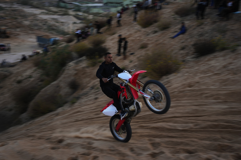 A Palestinian man rides his motorcycle on a sand dune in the Al-Zahra area, in the central Gaza Strip, Friday, Dec. 5, 2025. (AP Photo/Abdel Kareem Hana)