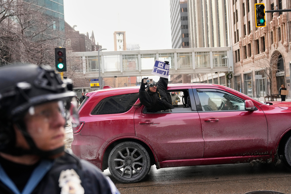 A protester holds a sign reading, "ICE Out," out of a car as she drives by Saturday, Jan. 17, 2026, in Minneapolis. (AP Photo/Yuki Iwamura)