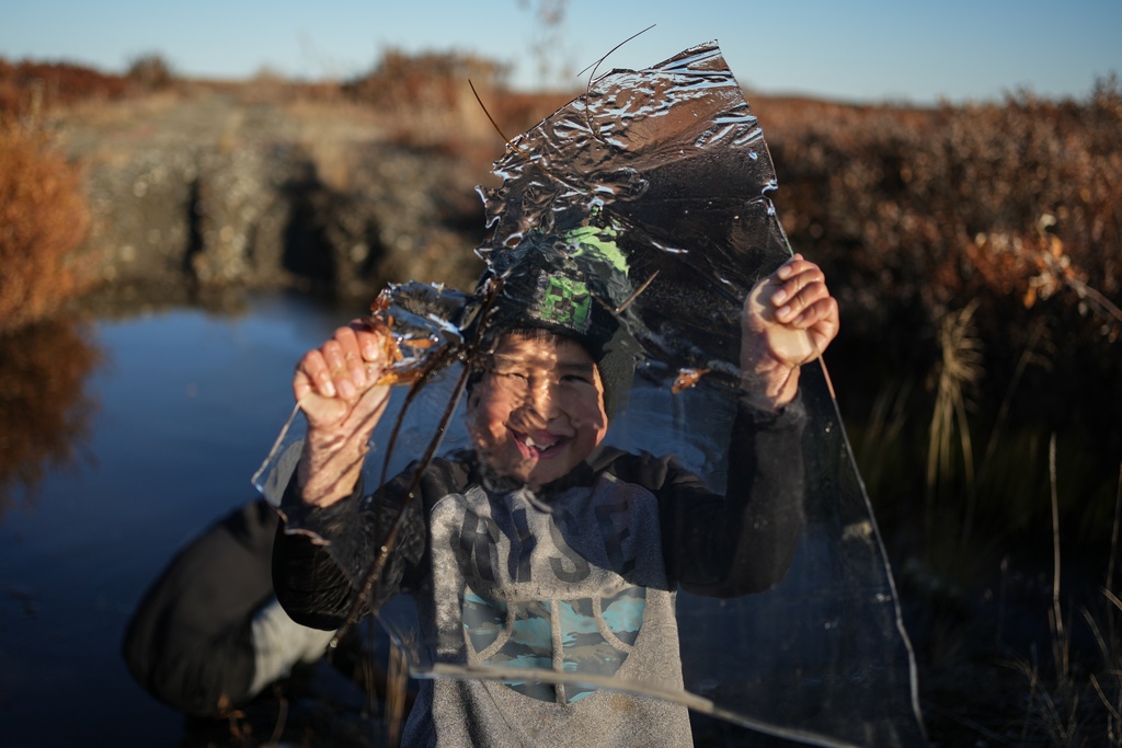 James Schaeffer, 7, plays with a slab of ice taken from a pond that formed on a warped road caused by thawing permafrost in Kotzebue, Alaska, Friday, Sept. 26, 2025. (AP Photo/Annika Hammerschlag)