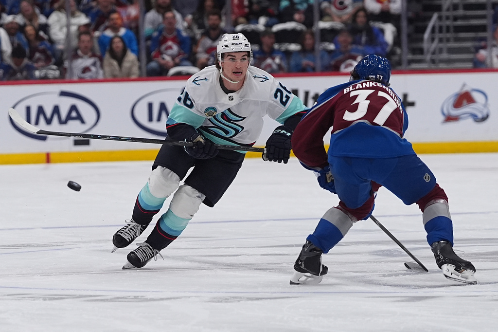 Seattle Kraken defenseman Joshua Mahura, left, drives past Colorado Avalanche defenseman Nick Blankenburg in the second period of an NHL hockey game Thursday, April 16, 2026, in Denver. (AP Photo/David Zalubowski)
