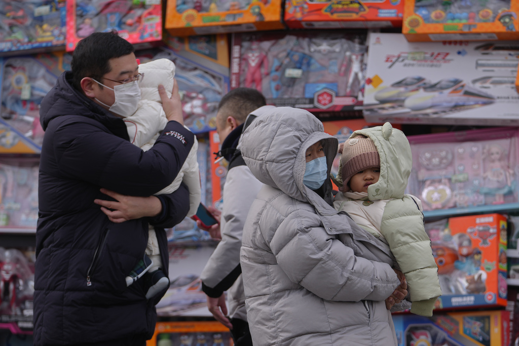 People carry their toddlers by a toy store in Beijing, Monday, Jan. 19, 2026. (AP Photo/Andy Wong)