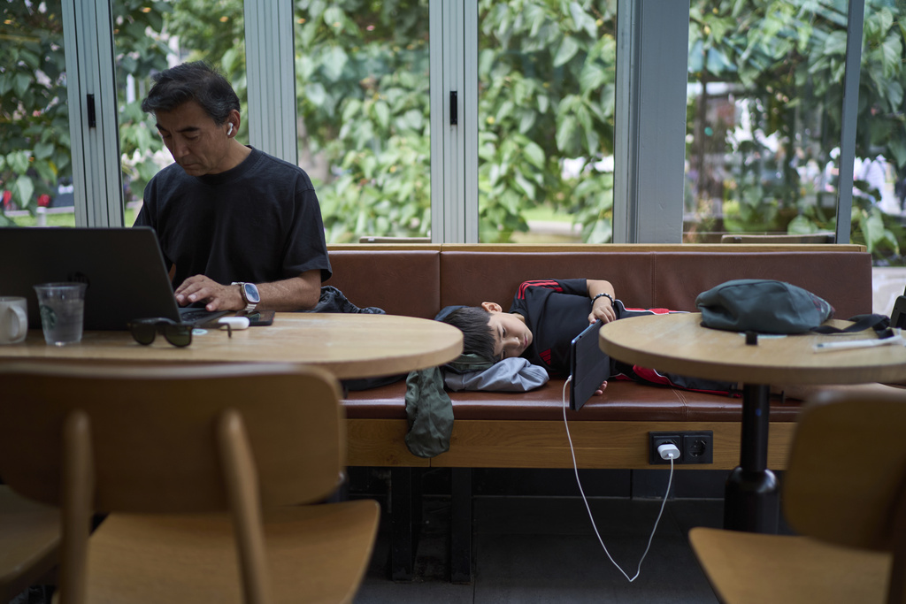 Former Xinjiang government engineer Nureli Abliz, works on an Uyghur-related rights project from a cafe as his son, Ilyon, 9, plays on a tablet in Mannheim, Germany, Wednesday, July 23, 2025. (AP Photo/David Goldman)