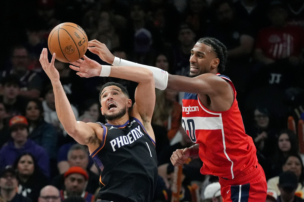 Phoenix Suns guard Devin Booker (1) and Washington Wizards center Alex Sarr battle for a loose ball during the first half of an NBA basketball game, Sunday, Jan. 11, 2026, in Phoenix. (AP Photo/Ross D. Franklin)