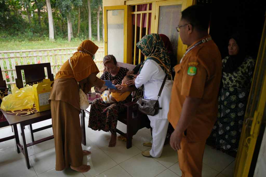 Health worker Siti Nurjanah, left, administers a measles vaccine to a child assisted by colleagues during a house-to-house measles vaccination campaign following an outbreak in Sumenep on Madura Island, Indonesia, Monday, Sept. 8, 2025. (AP Photo/Dita Alangkara)