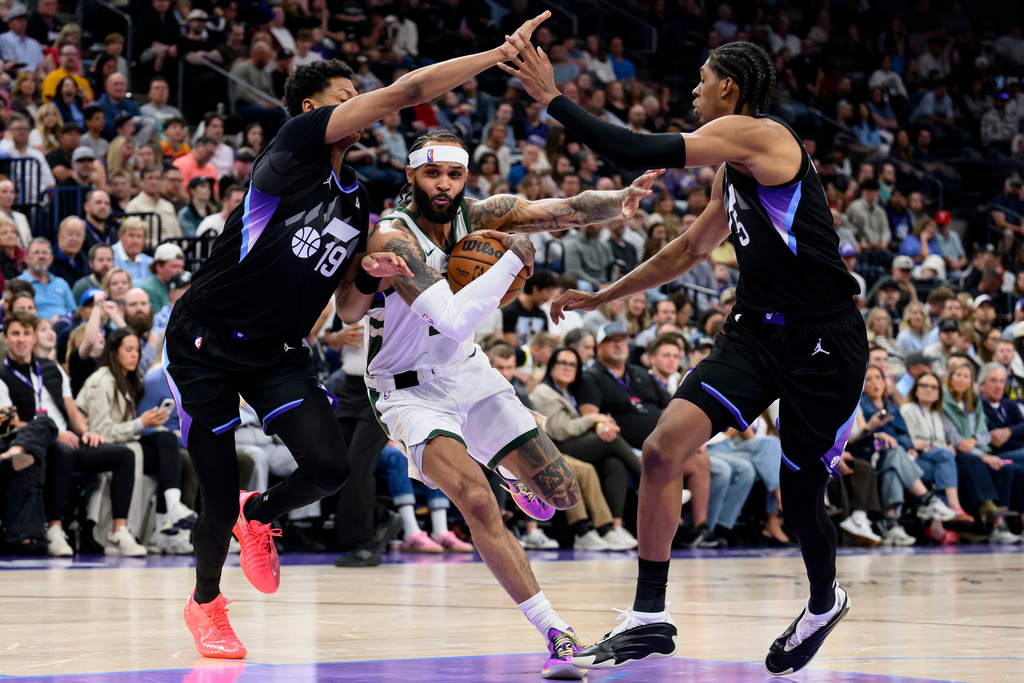 Milwaukee Bucks guard Gary Trent Jr., center, drives to the basket while guarded by Utah Jazz guard Ace Bailey, left, and forward Cody Williams, right, during the first half of an NBA basketball game Thursday, March 19, 2026, in Salt Lake City. (AP Photo/Tyler Tate)