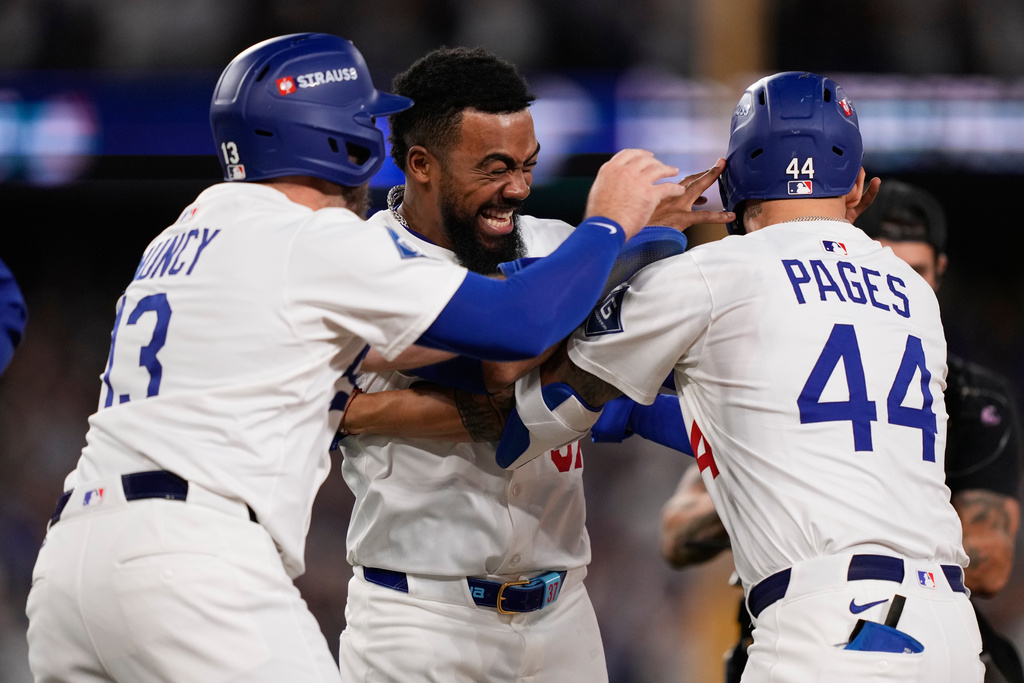 Los Angeles Dodgers' Andy Pages (44) is hugged by Teoscar Hernández, center, and Max Muncy after driving in the game-winning run on a ground ball and throwing error by Philadelphia Phillies relief pitcher Orion Kerkering during the eleventh inning in Game 4 of baseball's National League Division Series Thursday, Oct. 9, 2025, in Los Angeles. (AP Photo/Mark J. Terrill)
