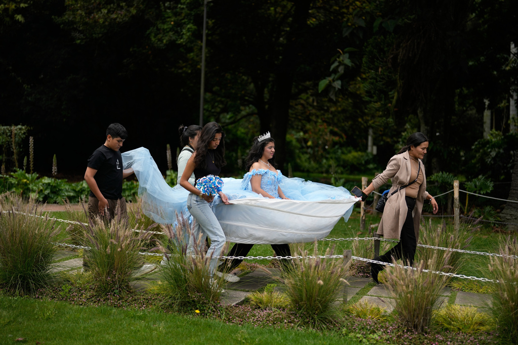 Relatives hold up the hem of quinceañera Gabriela Aragon's gown to keep it off the ground as they head to a photo session at the José Celestino Mutis Botanical Garden, in Bogota, Thursday, April 16, 2026. (AP Photo/Fernando Vergara)