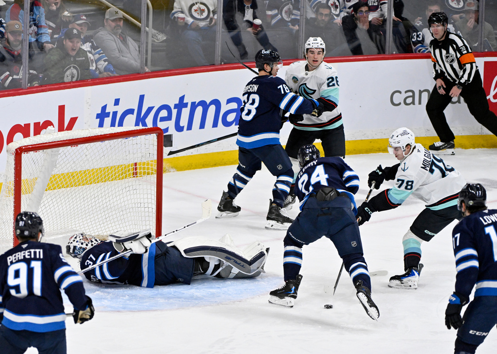 Seattle Kraken's Oscar Fisker Molgaard (78) tries to shoot against Winnipeg Jets goaltender Connor Hellebuyck (37) as Jets' Haydn Fleury (24) defends during second-period NHL hockey game action in Winnipeg, Manitoba, Monday, April 6, 2026. (Fred Greenslade/The Canadian Press via AP)