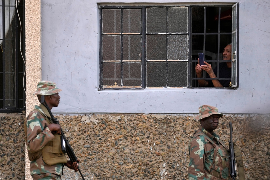 A resident uses a mobile phone to take a photograph of the South African National Defense Force officers deployed in the area, in the Riverlea township of Johannesburg, South Africa, Wednesday, March 11, 2026. (AP Photo/Themba Hadebe)