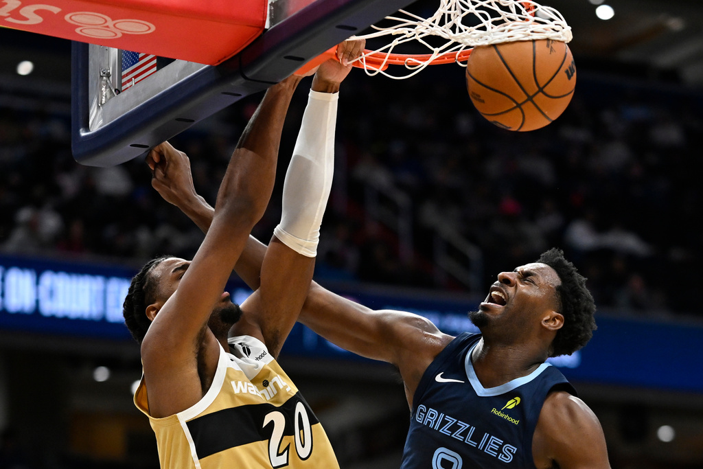 Washington Wizards center Alex Sarr (20) dunks the ball over Memphis Grizzlies forward Jaren Jackson Jr. during the first half of an NBA basketball game, Sunday, Dec. 28, 2025, in Washington. (AP Photo/John McDonnell)