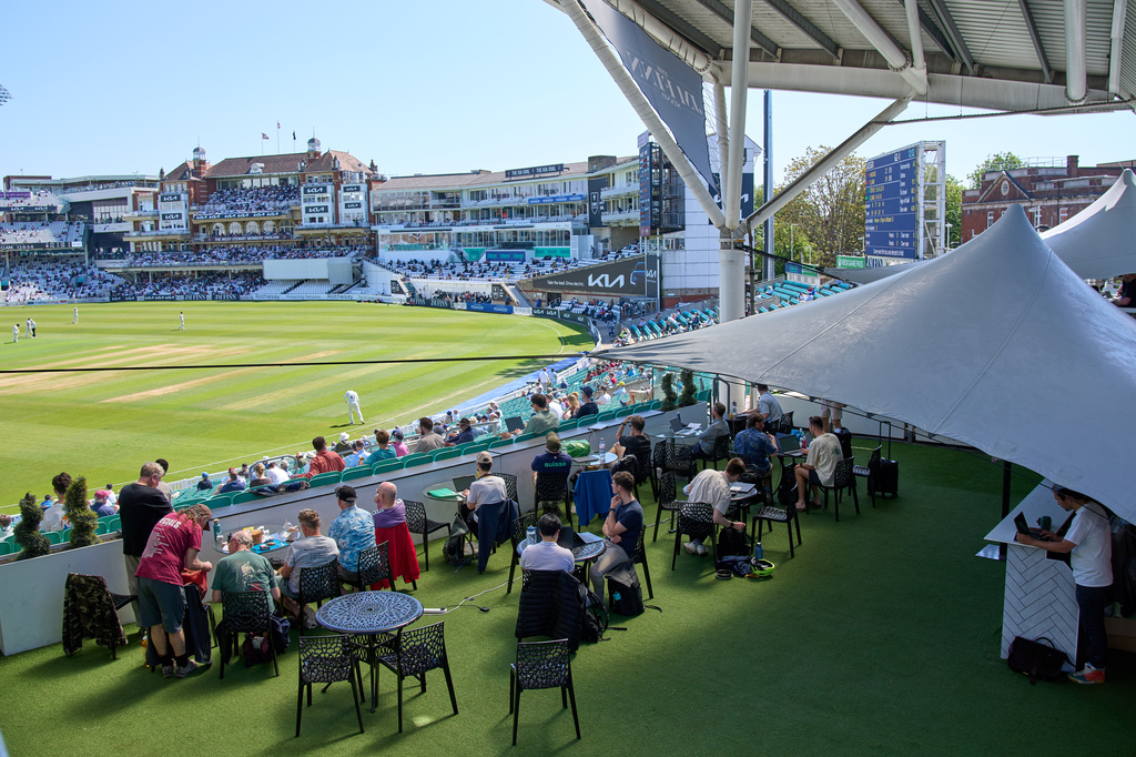 People work and watch cricket during a Surrey against Sussex County Championship cricket match at the Kia Oval in London, Friday, May 1, 2026. (AP Photo/Tony Hicks)