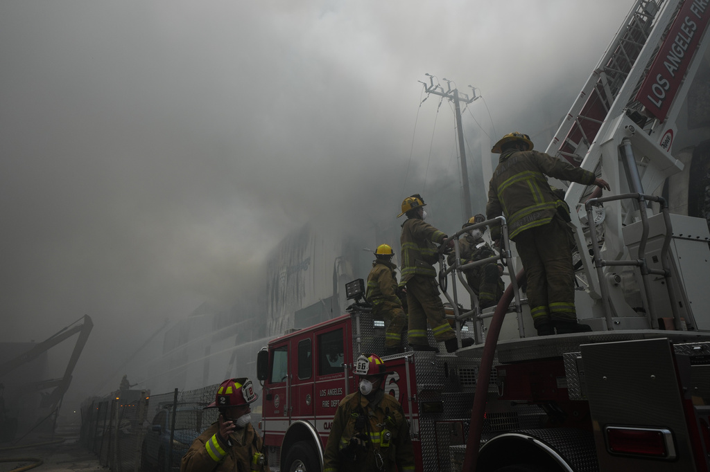 Firefighters work from a ladder truck while fighting a warehouse fire in the Boyle Heights neighborhood of Los Angeles, Sunday, June 21, 2026. (AP Photo/Jae C. Hong)