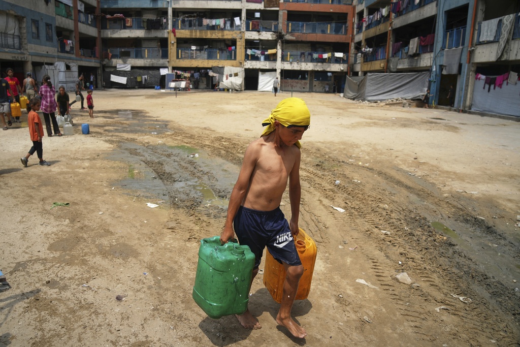In the summer heat, a Palestinian boy carries jerrycans after collecting water from a distribution point in Gaza City, Tuesday, Aug. 12, 2025. (AP Photo/Jehad Alshrafi)