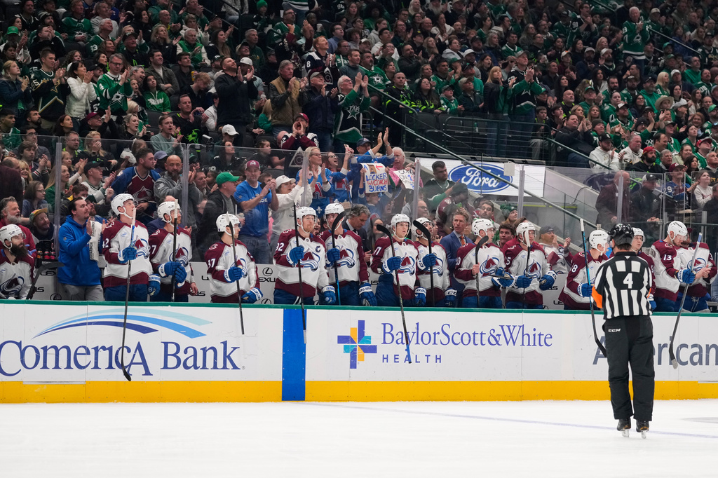 Fans and the Colorado Avalanche cheer after an in-house announcement celebrating Brent Burns', left sitting on bench, 1000th career game achievement in the first period of an NHL hockey game against the Dallas Stars, Saturday, April 4, 2026, in Dallas. (AP Photo/Tony Gutierrez)