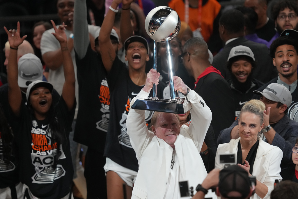 Las Vegas Aces owner Mark Davis, center, holds up the championship trophy after defeating the Phoenix Mercury in Game 4 of the WNBA basketball finals, Friday, Oct. 10, 2025, in Phoenix. (AP Photo/Rick Scuteri)